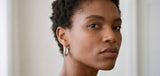Close-up of a woman wearing gold Holly Hoop earrings with a neutral background from Delani Jewelry