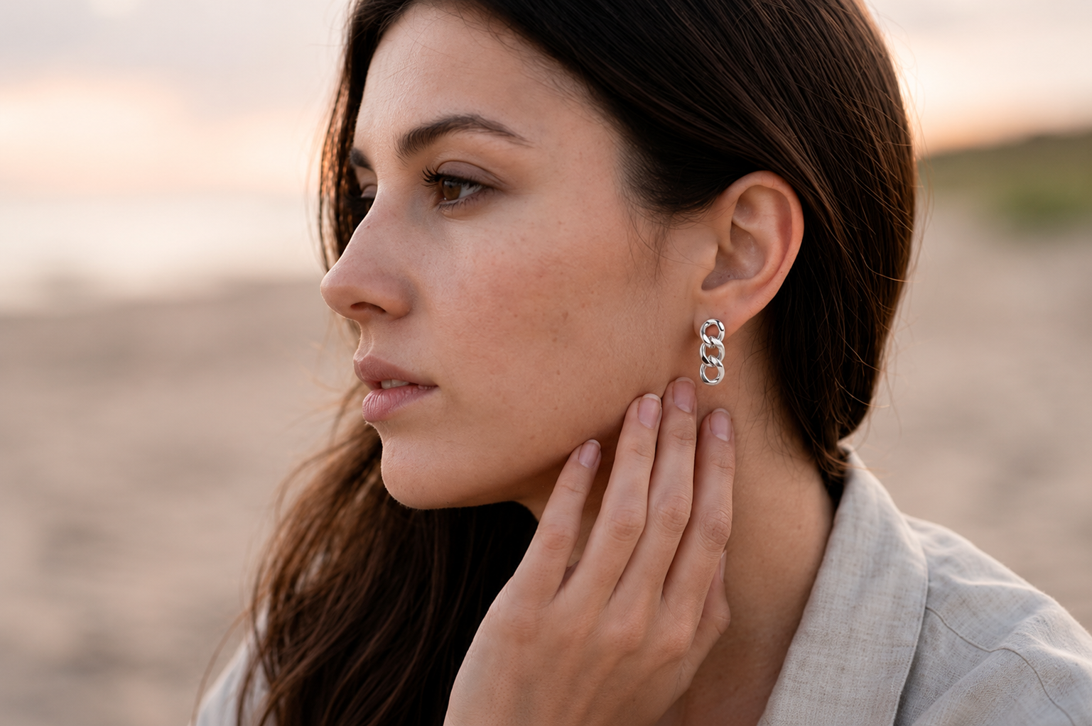 A woman in profile wearing a silver Alba earrings photographed outdoors against a softly blurred sandy background at sunset.