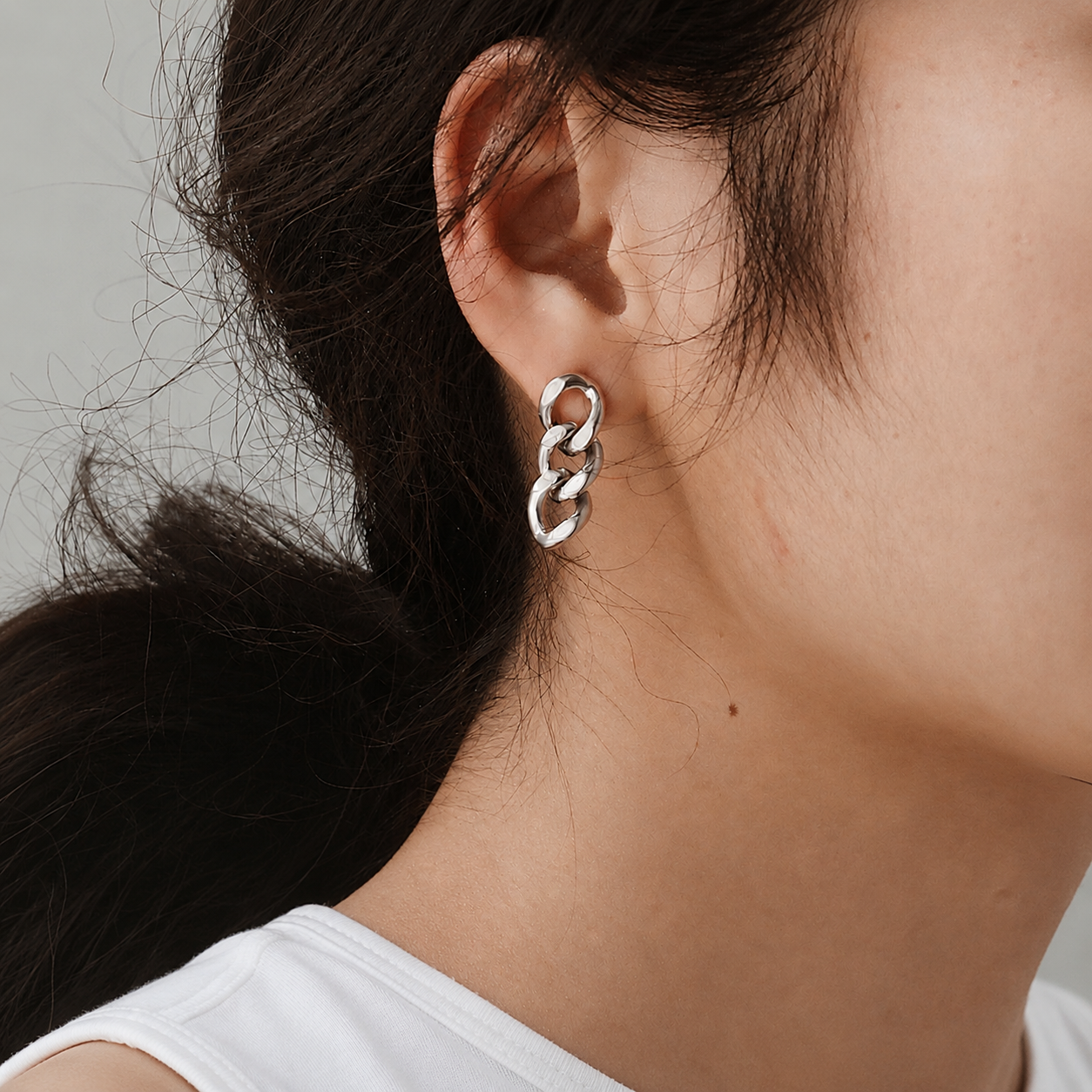 A close-up of a person's ear wearing a polished silver dangle earring bt Delani Jewelry composed of three interlocking oval links named the Alba earrings.