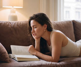 Woman reading a book on a couch in a cozy living room wearing Holly Hoop earrings from Delani Jewelry
