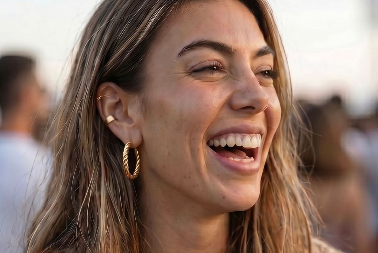 Woman laughing at the beach wearing the waterproof Kenza Cuff, tarnish-proof gold jewelry with lifetime color guarantee.