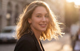Woman with blonde hair smiling outdoors with a blurred background wearing Frankie Hoops from Delani Jewelry