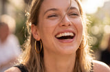 Woman laughing outdoors with a blurred background wearing Frankie Hoops from Delani Jewelry