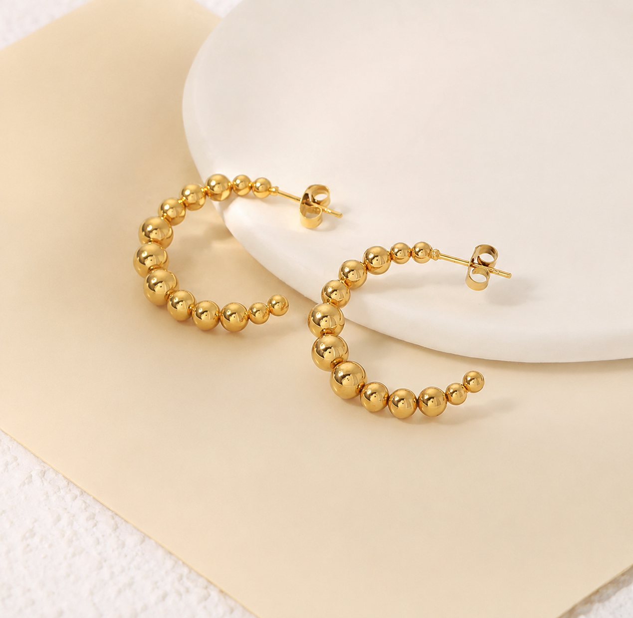 Gold hoop earrings on a white plate with a beige background from Delani Jewelry