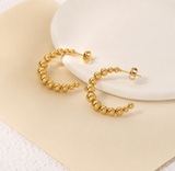 Gold hoop earrings on a white plate with a beige background from Delani Jewelry