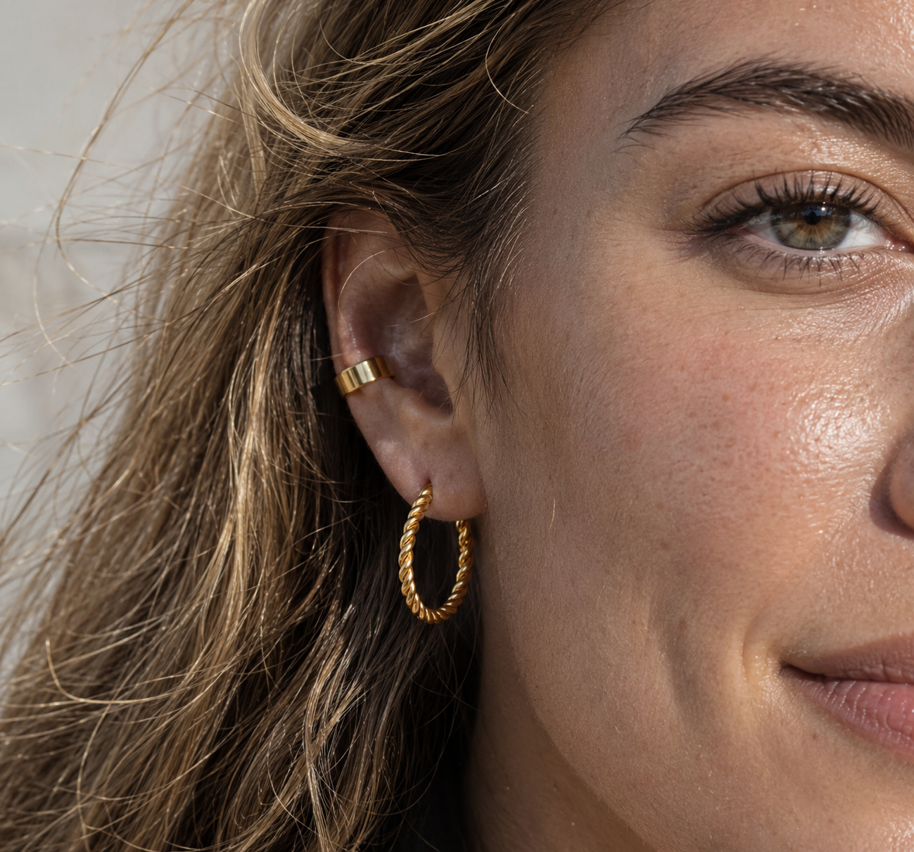 Close-up of model's ear wearing the gold Kenza Cuff with twisted hoop earring, waterproof and tarnish-proof