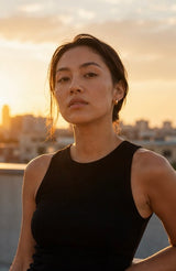 Woman in a black sleeveless top standing against a sunset cityscape wearing Naji Earrings by Delani Jewelry