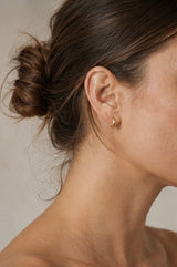 Close-up of a person wearing a gold Naji earring with a neutral background from Delani Jewelry