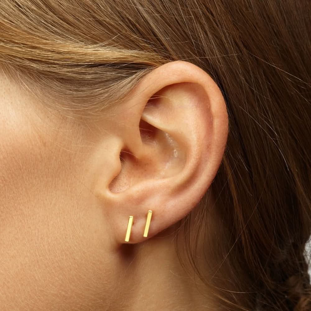 Close-up of Delani Jewelry gold bar stud earrings styled in first and second lobe piercings, showcasing minimalist geometric earrings with a polished finish. Named Namaari Studs