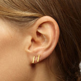Close-up of Delani Jewelry gold bar stud earrings styled in first and second lobe piercings, showcasing minimalist geometric earrings with a polished finish. Named Namaari Studs