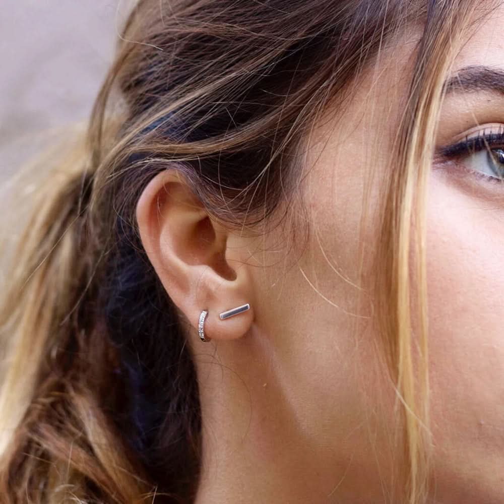 Close-up of Delani Jewelry silver bar stud earrings paired with a silver huggie hoop, showcasing minimalist geometric earrings perfect for first, second, or third lobe piercings and everyday wear. Named Namaari Studs