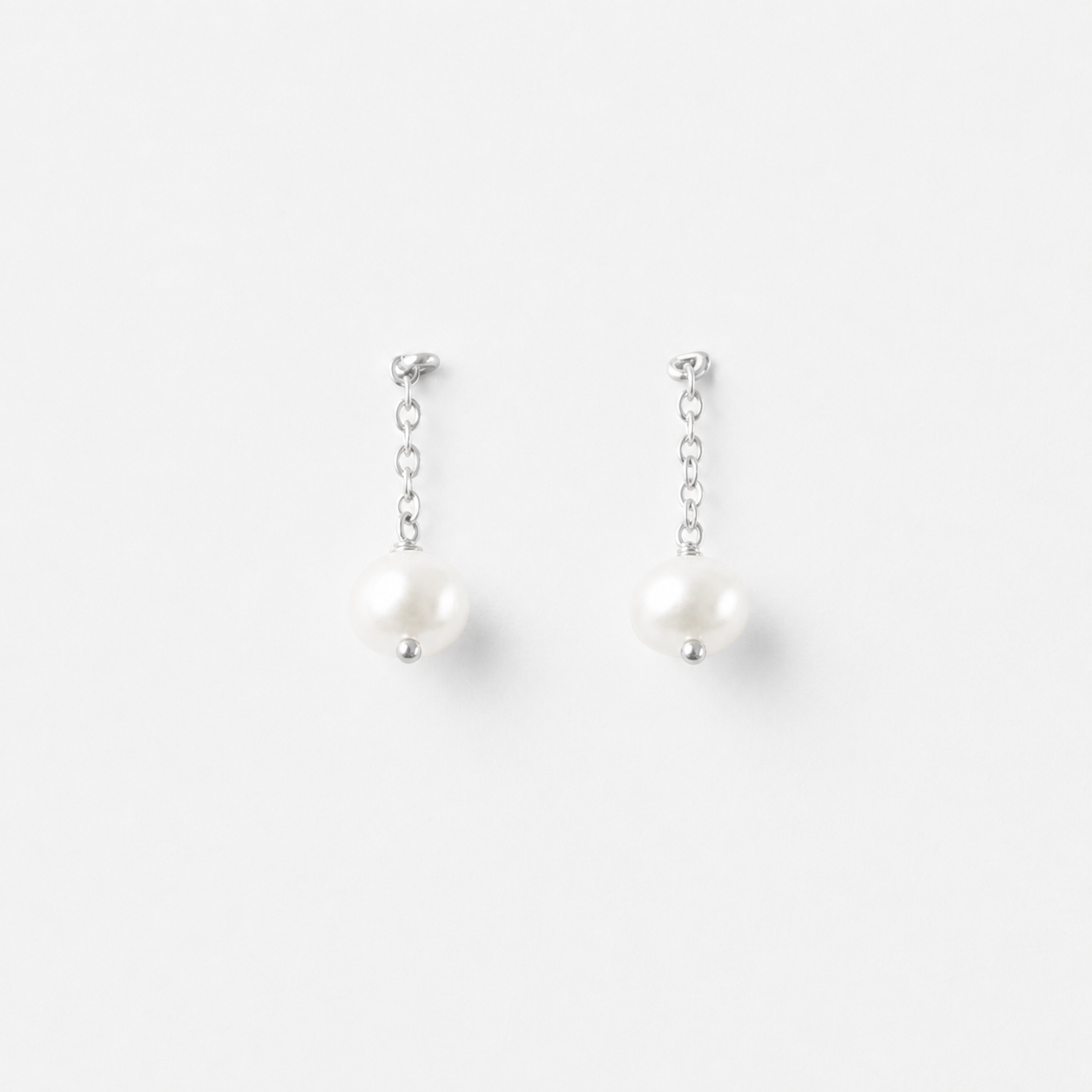 Minimalist product photo of Delani Jewelry Nubia Short Pearl Earrings in silver with luminous freshwater pearls. Tarnish-free, waterproof earrings backed by a lifetime color guarantee.