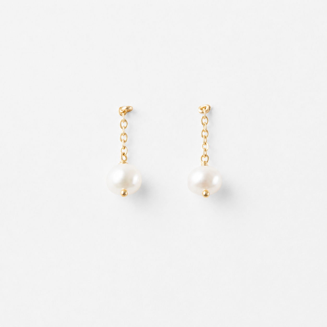 Product image of Delani Jewelry Nubia Short Pearl Earrings in gold with classic freshwater pearl drops. Tarnish-free, waterproof stainless steel earrings with a lifetime color guarantee.