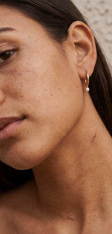Close-up of a person wearing Pola Earrings in gold with a pearl accent from Delani Jewelry