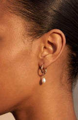 Close-up of an ear wearing a gold hoop earring with a pearl pendant wearing Pola Hoops by Delani Jewelry