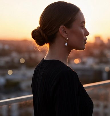 Woman with a bun and Pola pearl earring against a blurred cityscape at sunset from Delani Jewelry