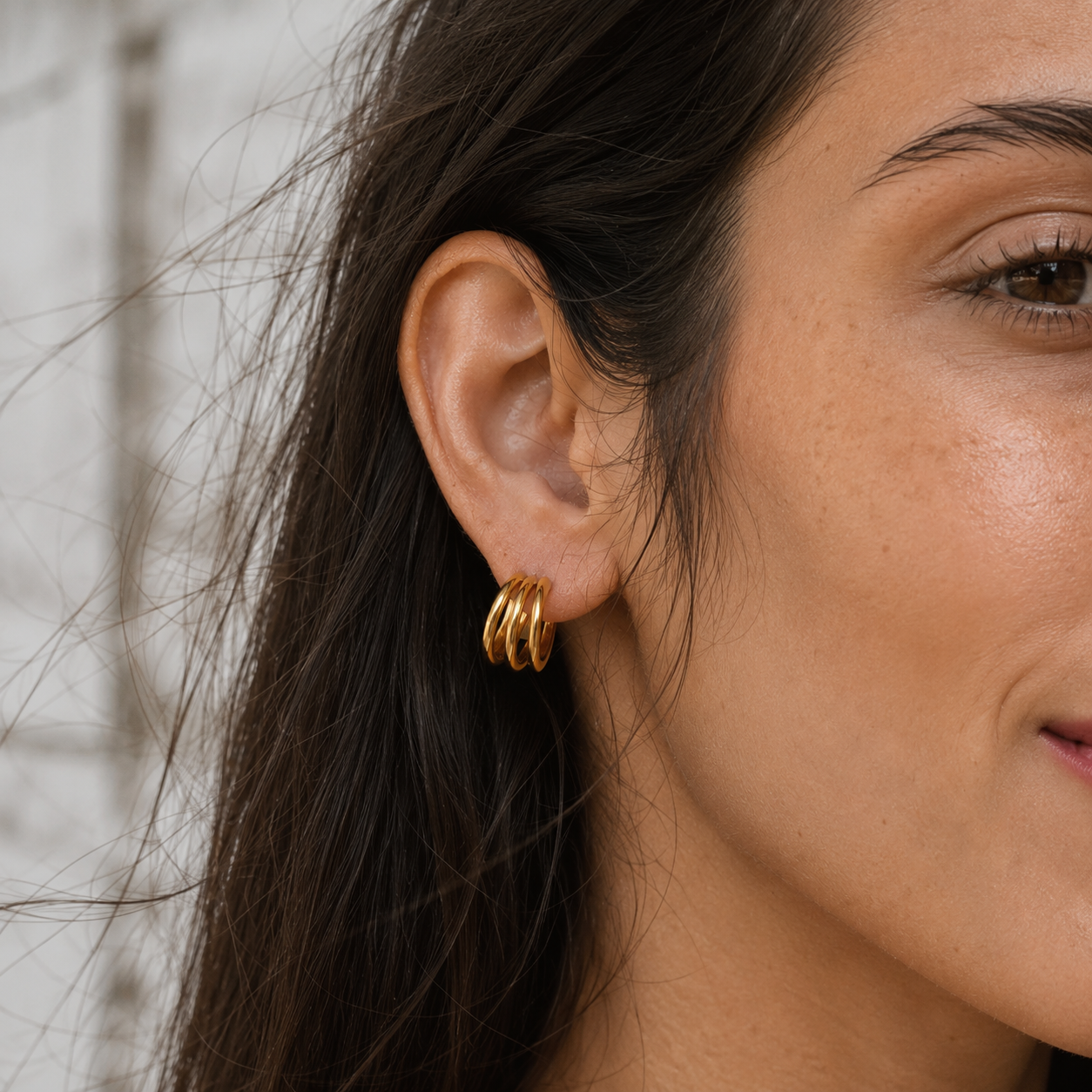 Editorial close-up of Delani Jewelry Saja Hoop Earrings in gold featuring a polished triple-hoop design. Waterproof, tarnish-proof, and protected by a lifetime color guarantee.
