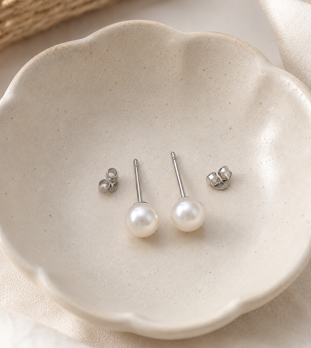 Satya pearl stud earrings from Delani Jewelry in a ceramic dish with stainless steel posts and butterfly backs, waterproof, tarnish-proof, hypoallergenic, and backed by a lifetime color guarantee.