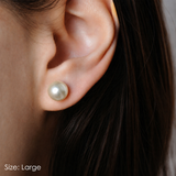 Close-up of an ear wearing a pearl earring with dark hair partially visible. Size Large. Classic Satya pearl earrings from Delani Jewelry with luminous white pearls, stainless steel posts, waterproof and tarnish-proof design, perfect for everyday wear with a lifetime color guarantee.
