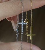 Two necklaces with cross pendants, one silver and one gold, held against a neutral background to showcase color choices. From Delani Jewelry