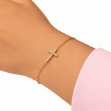 Gold bracelet with a cross on a wrist against a white background from Delani Jewelry
