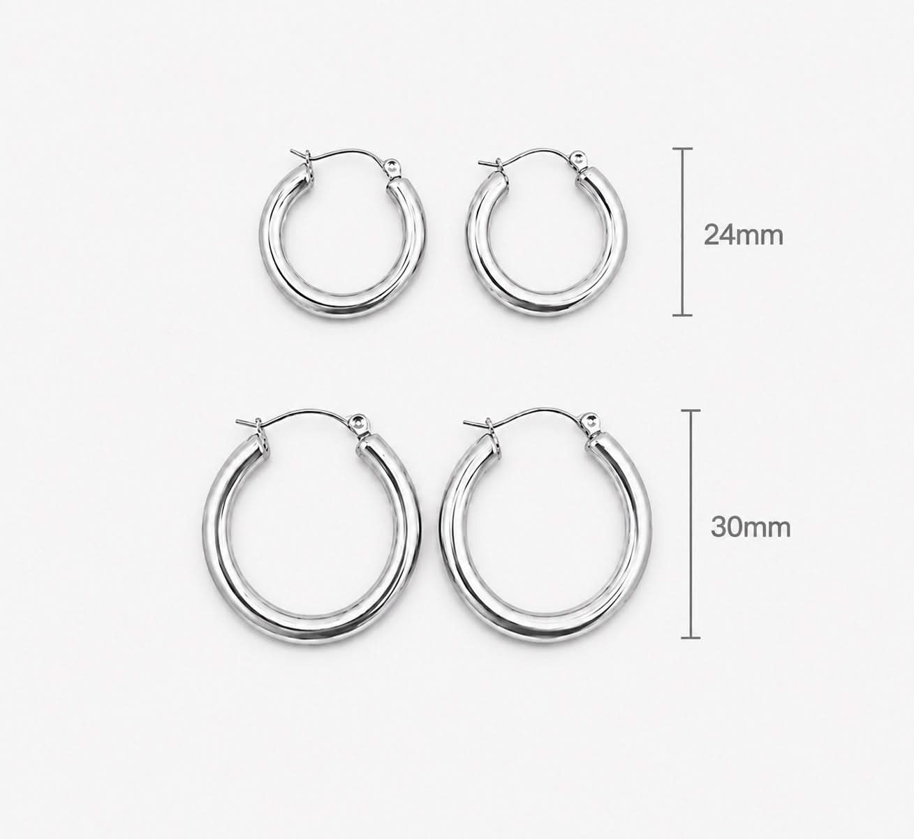 Two pairs of silver hoop earrings shown on a light gray background, with size labels indicating 24mm and 30mm diameters. Delani Jewelry Holly silver hoop earrings with a bold rounded silhouette and high-polish finish, designed to elevate any look from day to night. Waterproof, tarnish-proof, hypoallergenic, and backed by our Lifetime Color Guarantee.