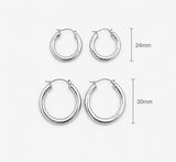 Two pairs of silver hoop earrings shown on a light gray background, with size labels indicating 24mm and 30mm diameters. Delani Jewelry Holly silver hoop earrings with a bold rounded silhouette and high-polish finish, designed to elevate any look from day to night. Waterproof, tarnish-proof, hypoallergenic, and backed by our Lifetime Color Guarantee.